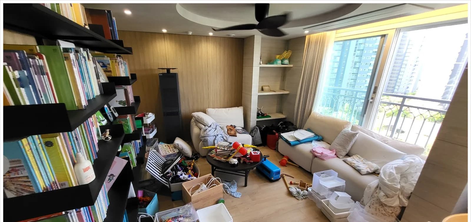 정리 전 거실. 바닥에 책과 상자, 장난감이 흩어져 있다